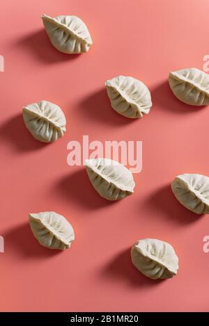 Halbfertigprodukte auf pinkfarbenem Hintergrund. Draufsicht auf Manti oder Knödel. Muster. Stockfoto