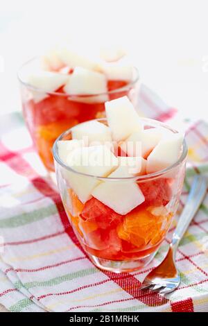 Gesundes, erfrischendes, farbenfrohes Dessert mit geschnittenen frischen Früchten, serviert auf gläsernen Tassen mit Gabel auf Leinentuch vor weißem Hintergrund Stockfoto