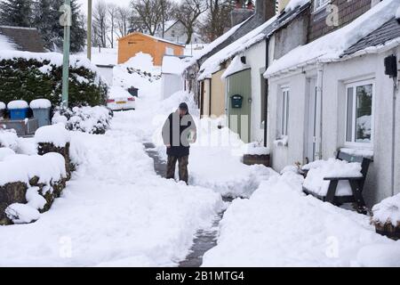 Ein Mann geht eine schneebedeckte Straße im Dorf Leadhills, South Lanarkshire, Schottland hinunter. Stockfoto