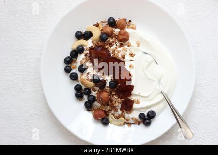 Platte aus griechischem Joghurt mit Granola, Nüssen, Datteln und Blaubeeren. Gesundes Frühstückskonzept. Stockfoto