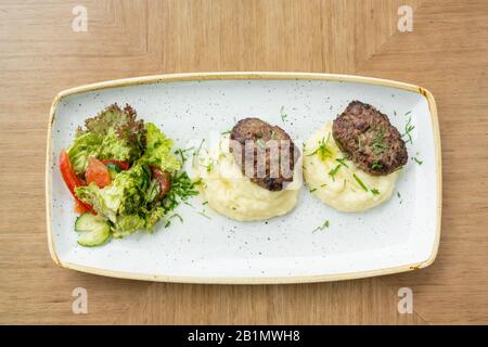 Köstliche saftige Fleischstückchen, Kartoffelpüree mit Grüns und frischem gesundem Salat von Tomaten und Salatblättern. Stockfoto