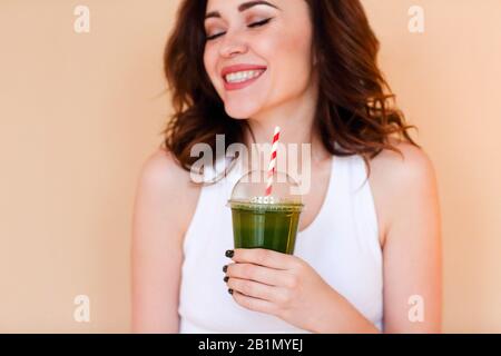 Crop freute junge Frau mit grünem Smoothie vor Wandhintergrund lachen Stockfoto