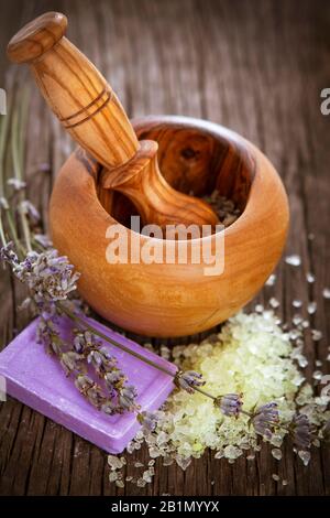 Von oben mit natürlicher, handgefertigter Seife mit Lavendel und Meersalz neben Holzmörtel mit Pfirsich auf Holzgrund Stockfoto