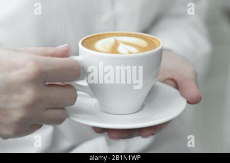 Frau Hände halten Tasse heißen Kaffee Latte Cappuccino mit üppigem Milchschaum herzförmig. Stockfoto