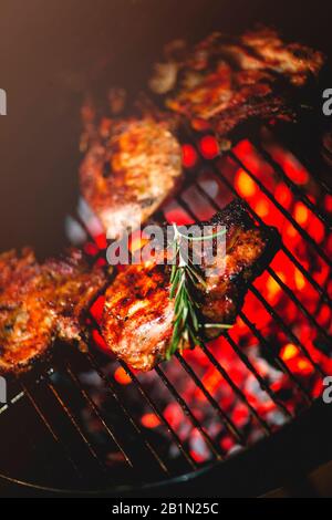 Von oben köstlichen, appetitlichen Fleischsteaks mit frischen Rosmaringrillen auf dem Regal über brennenden Kohlen Stockfoto