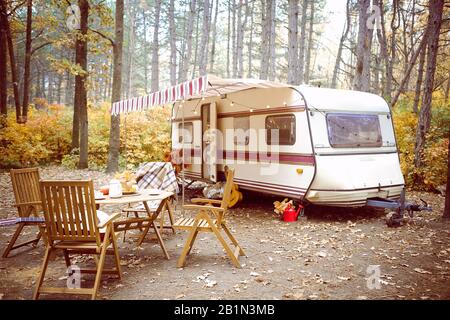 Holzstühle und Tisch mit Teeset außerhalb der gemütlichen Retro-Karawane am Herbsttag in ruhiger Landschaft Stockfoto