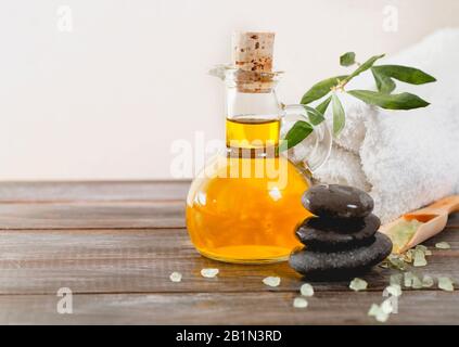 Weiches Handtuch auf dem Holztisch in der Nähe von frischem Olivenöl und Salz im Spa-Salon Stockfoto