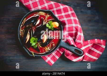 Draufsicht auf eine Schüssel köstlicher Suppe mit Garnelen und Muscheln, die in der Nähe von Serviette auf dem Tisch im Restaurant platziert werden Stockfoto
