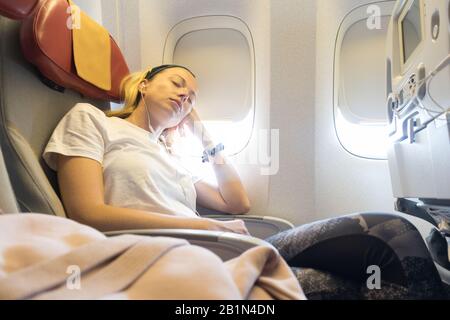 Müde blonde casual kaukasische Dame nappt auf unbequem Sitz, während sie mit dem Flugzeug unterwegs ist. Stockfoto