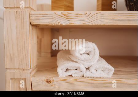 Drei verdrehte weiße Mohair-Handtücher auf einem Holzregal in der Badewanne. Stockfoto