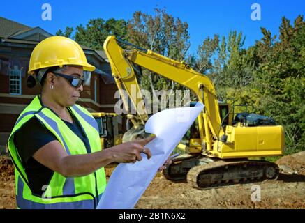 Lesepläne für Frauen, Latino, Schwarz, amerikanische Ureinwohner auf der Baustelle vor Ort und Bulldozern Stockfoto