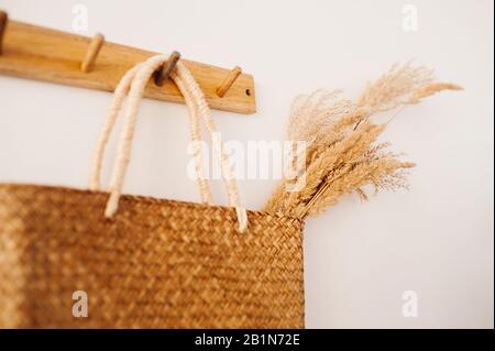 Wiederverwendbarer, umweltfreundlicher gewebter Sack mit Stringbeutel, an dem ein Blumenstrauß aus Weizen oder Ohren an einem Holzhaken an einer weißen Wand hängt Stockfoto