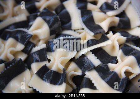 Nahaufnahme einer Platte voller gekochter Pasta in Form von zweifarbigen Krawatten und Meeresfrüchtegeschmack, schwarz und weiß Stockfoto