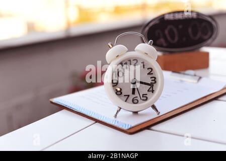 Weiße Alarm Clock mit Drehscheibe auf dem Tisch in einem Restaurant mit einer Reservierung Anmelden am Morgen oder zum Abendessen für eine Diät Stockfoto