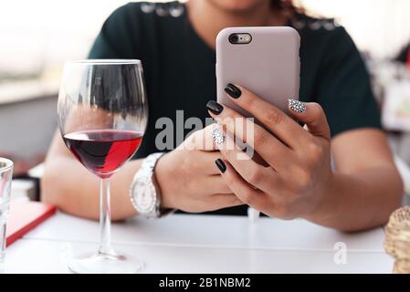 Schönes Mädchen mit Telefonhänden im Restaurant mit einem Glas Rotwein mit Uhr und Schrift Stockfoto