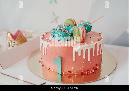 Rosa schöner großer Kuchen mit grüner Nummer eins, dekoriert mit Lebkuchen und Makronen Stockfoto