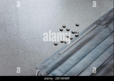 Kleine runde Tabletten ohne Verpackung mit blauer medizinischer Atemmaske auf grauem glänzenden Hintergrund, flacher Lay, Draufsicht Stockfoto