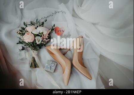 Stilvolles Zubehör der Brautpappe für Kleidung und Hochzeit, beige Lacklederschuhe, silberfarbene Schachtel für Ringe und ein stilvoller Blumenstrauß aus Pony Rose Stockfoto