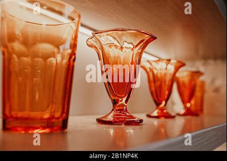 Identische, elegante, strukturierte Brille und Vasen aus hellorangefarbenem Glas für Getränke stehen auf Holzböden im Inneren des Raumes Stockfoto