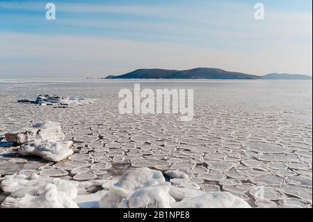 Winterlandschaft, kaltes gefrorenes Meer mit kleinen runden Eiszapfen, blauer klarer Himmel vor der Kulisse von Bergen und schneebedeckten Hügeln Stockfoto