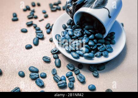 Weißer Becher voller Kaffeebohnen fiel und bestreute Kaffeebohnen in klassischer blauer Farbe Stockfoto
