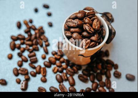 Vorgefertigte Bilder für die Kaffeewerbung und zur Veröffentlichung bereit, eine große Anzahl gerösteter Kaffeebohnen wird um einen weißen Becher voller b verstreut Stockfoto