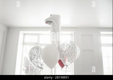 Ein Haufen weißer und silberner Luftballons und eine große Silber-Folie Nummer eins in einem weißen Raum Stockfoto