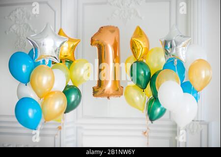 Ein Haufen mehrfarbiger Ballons und eine große Goldfolie Nummer eins in einem weißen Raum und Foliensterne Stockfoto
