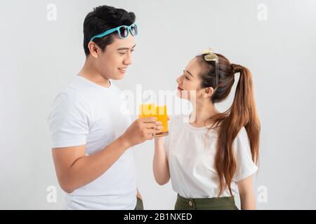 Schönes junges Paar, isoliert über weißem Hintergrund stehend, mit einer Brille mit Orangensaft Stockfoto