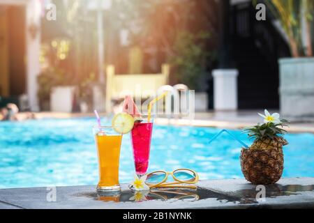 Sommerurlaub tropisches Konzept. Frischer Orangensaft und Wassermelonsaft und Ananas an der Grenze eines Schwimmbades. Stockfoto