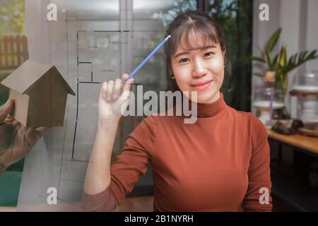 Doppelbelichtung des weiblichen Architekten, der mit einem neuen Startup-Projekt im Heimbüro mit Hausmodell und Blaupause arbeitet. Stockfoto