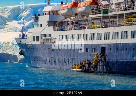 Passagiere, die von einem Zodiac aus auf einem blau-weißen Expeditionschiff in der Antarktis verladen werden Stockfoto