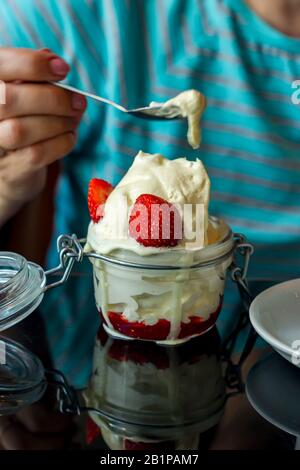 Frau, die Vanilleeis mit Erdbeersauce in einem Glas isst Stockfoto