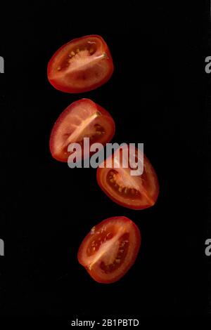 Kirschtomaten. Vier Scheiben Kirschtomaten in schwarzer Steinplatte. Stockfoto