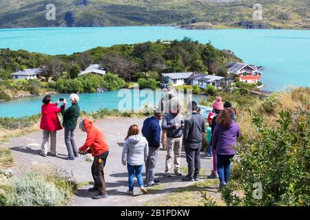 Touristen über dem Lake Pehoe und der Pehoe Lodge im Nationalpark Torres del Paine, Patagonien, Chile, deren Gewässer durch glaziale Felsblumen verfärbt sind Stockfoto