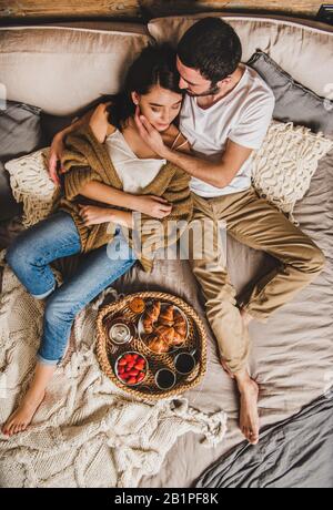 Glückliches Paar, das im Bett frühstücken und sich umarmen kann Stockfoto