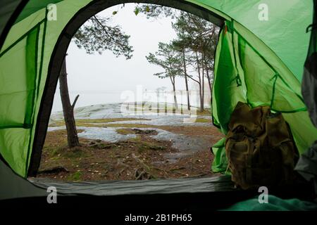 Blick von innen auf ein Touristenzelt mit Rucksack. Schöne skandinavische Landschaft mit Wald und felsigen Ufer. Finnland Stockfoto