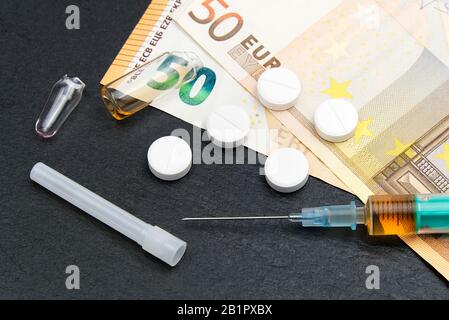 Geld und Pillen mit Drogen und einer Spritze auf Schwarz Stockfoto