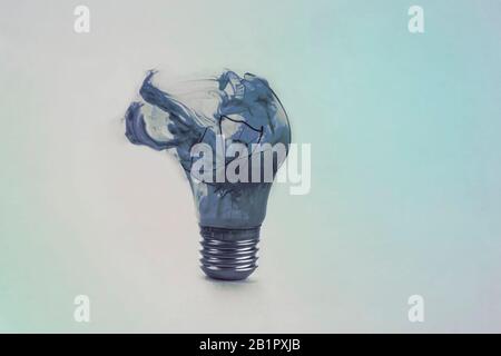 Eine defekte Glühlampe auf blauem Grund mit Rauch. Überfälliges Ideenkonzept. Welt nicht elektrisch. Erdstunde. Stockfoto