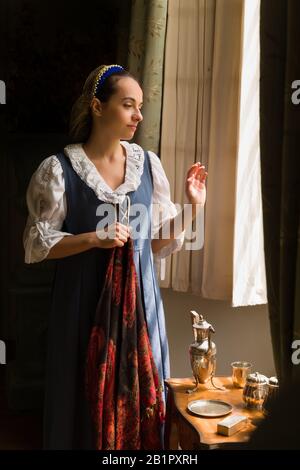 Hübsche junge Frau in der Renaissance kostüm Blick durch das Fenster einer Eigenschaft freigegeben Authentische mittelalterliche Schloss in Frankreich Stockfoto