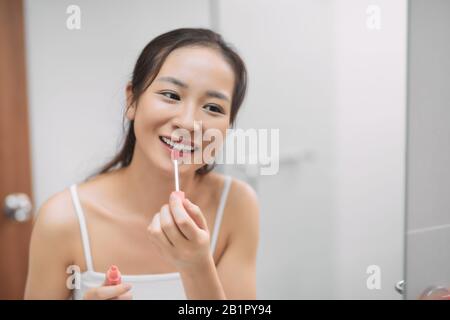 Schöne asiatische Frau, die Spiegel sieht und Lippen-Make-up-Lippenstift in der Toilette des Pulverzimmers auftragen Stockfoto