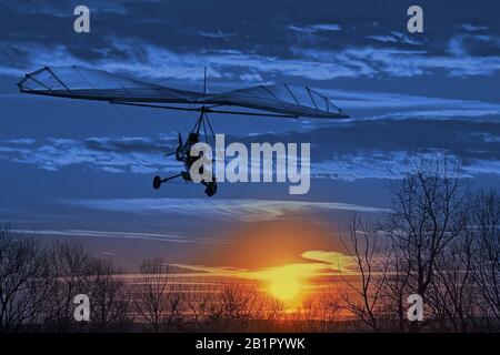 Der motorisierte Drachenflieger fliegt im Sonnenuntergang. Classic Blue Pantone 2020 Jahresfarbe. Stockfoto