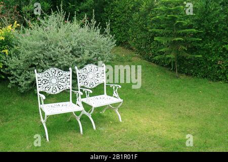 Ein Paar weiße schmiedeeiserne Stühle im alten Stil im grünen Garten Stockfoto