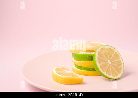 Frische leckere Zitronen- und Limonen-Zitrusfrüchte-Scheiben auf pinkfarbener Platte gestapelt, minimaler Hintergrund isoliert, Winkelansicht, Makro Stockfoto