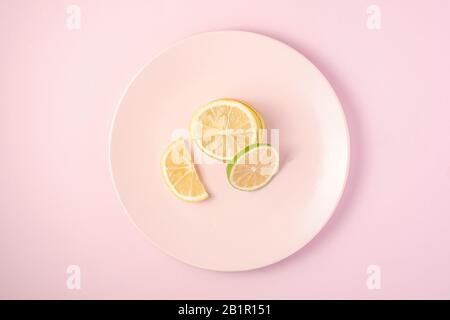 Frische leckere Zitronen- und Limonen-Zitrusfrüchte-Scheiben auf pinkfarbener Platte, minimaler Hintergrund isoliert, Draufsicht Stockfoto