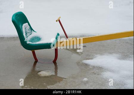 Schnee auf dem Spielplatz für Kinder geschmolzen. Grüner Sitz mit Schneedecke Stockfoto