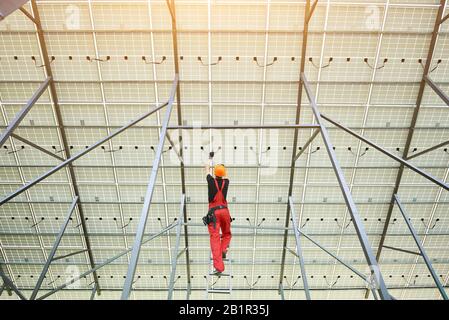 Installation und Verdrahtung von Solar-Lichtschäften. Rückansicht des Mitarbeiters in orange gleichförmige verbindende Sonnenkollektoren an der Station. Konzept zur ökologischen Energieeinsparung. Stockfoto