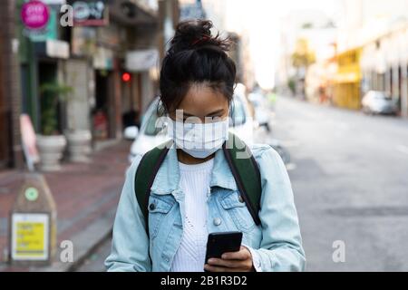 Frau, die auf der Straße spaziert und eine Gesichtsmaske aus dem Corona-Virus trägt Stockfoto