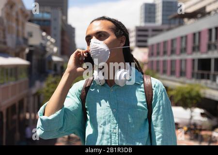 Gemischter Rennmann, der sein Telefon verwendet, während er eine Maske trägt Stockfoto