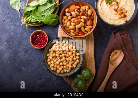Gekochte Nierenbohnen, weiße Bohnen, Kichererbsen und hausgemachter Hummus auf einem Teller, Steinhintergrund Stockfoto